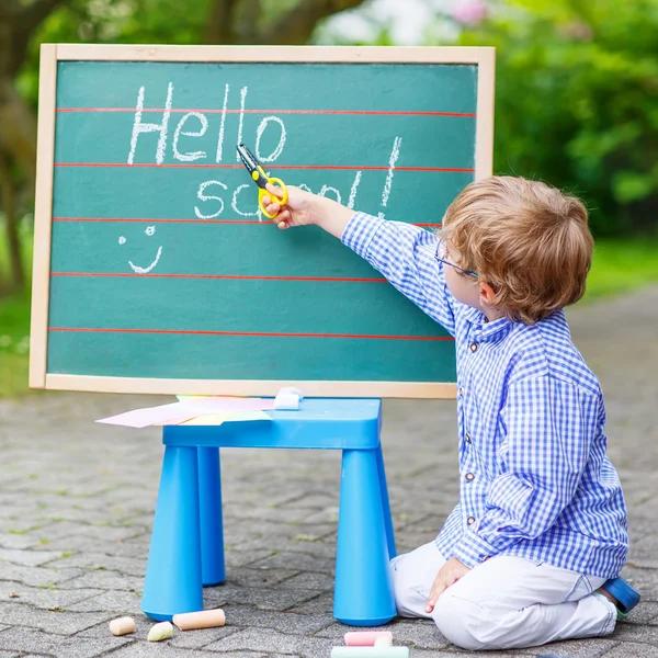 Cute little kid boy with glasses at blackboard practicing writin — Stock Photo, Image