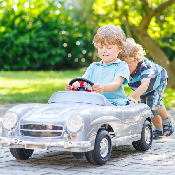 Zwei lustige kleine Freunde spielen mit großen alten Spielzeugautos — Stockfoto