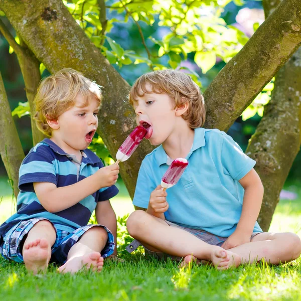 Zwei kleine Geschwister essen rotes Eis im heimischen Garten. — Stockfoto