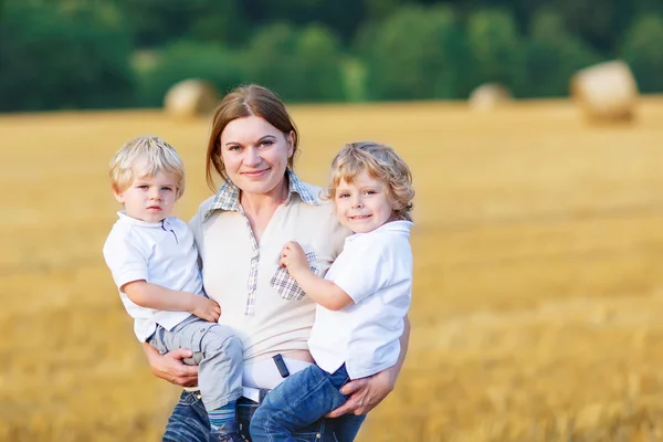 Jeune mère et deux petits jumeaux garçons s'amusent sur le foin jaune — Photo