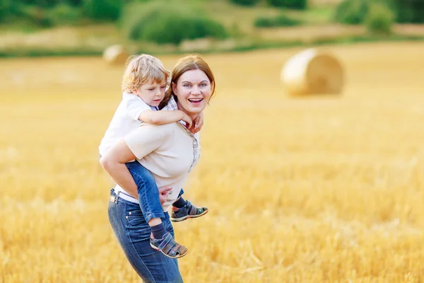 Junge Mutter und ihr kleiner Sohn amüsieren sich auf gelbem Heufeld — Stockfoto