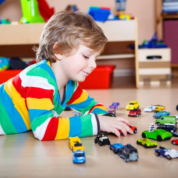 Boldog vicces kis szőke gyermek játszó rengeteg játékszert autók — Stock Fotó