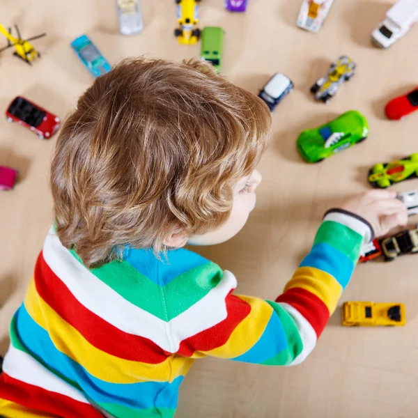 Pequena criança loira brincando com muitos carros de brinquedo interior — Fotografia de Stock