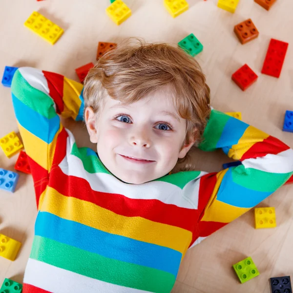 Маленький блондин играет с кучей разноцветных пластиковых блоков — стоковое фото