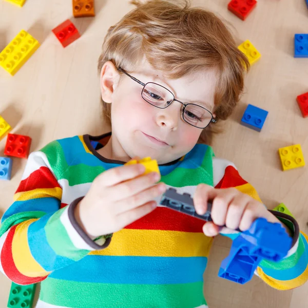 Маленький блондин играет с кучей разноцветных пластиковых блоков — стоковое фото