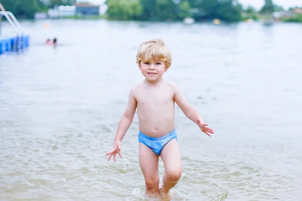 Pequeño chico rubio divirtiéndose con salpicaduras en un lago, outdoo — Foto de Stock