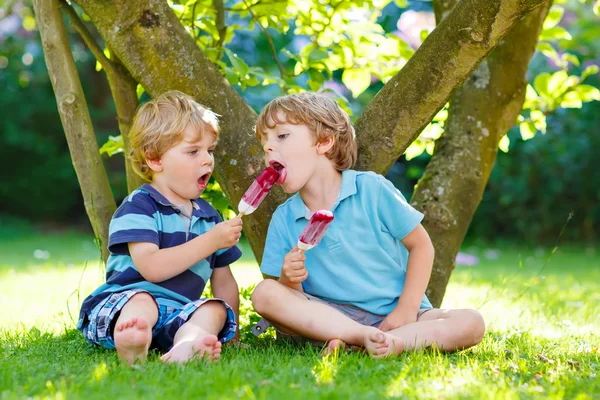 Zwei kleine Geschwister essen rotes Eis im heimischen Garten. — Stockfoto