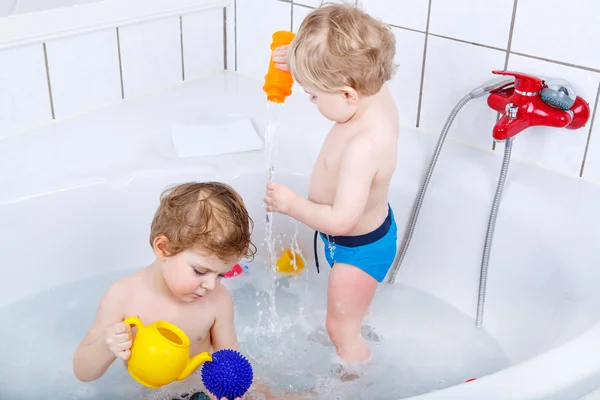 Два маленьких сидящих мальчика веселятся с водой, принимая ванну в — стоковое фото