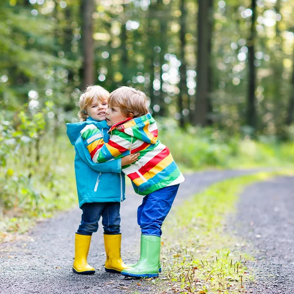 Two little sibling boys in colorful raincoats and boots walking — Stock Photo, Image