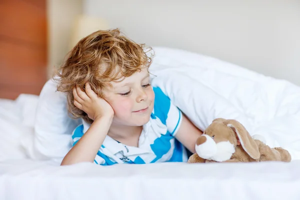 Adorável garoto depois de dormir em sua cama branca com brinquedo — Fotografia de Stock