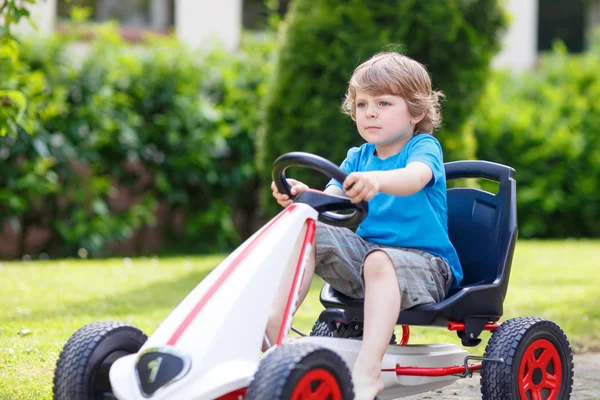 Активный маленький мальчик весело и за рулем игрушечного гоночного автомобиля — стоковое фото