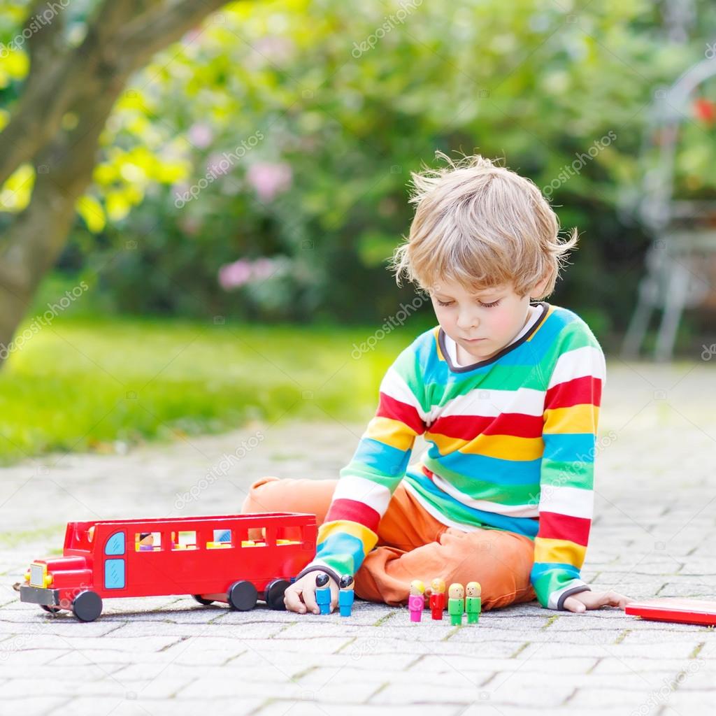 Active kid boy playing with red school bus and toys