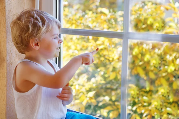 Petit garçon de trois ans regardant par la fenêtre sur jaune au — Photo