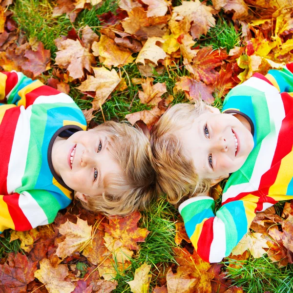 Two little kid boys laying in autumn leaves in colorful clothing — Stock Photo, Image