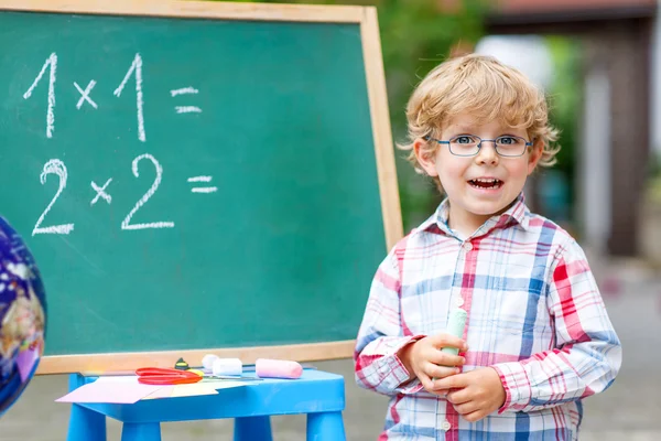 Cute little kid boy with glasses at blackboard practicing mathem — Stock Photo, Image