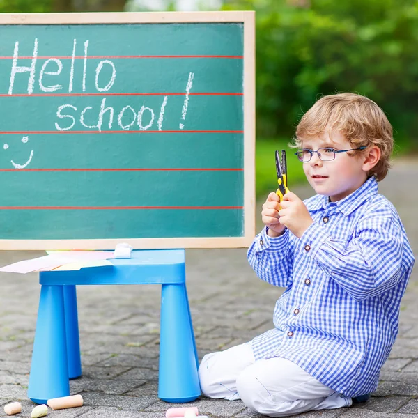 Petit garçon mignon avec des lunettes au tableau noir pratiquant l'écriture — Photo