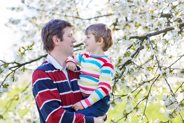 Unga far och Lille unge pojken i blommande trädgård — Stockfoto