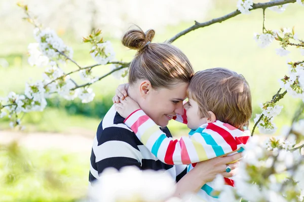 Ung mamma och lilla kid boy roar sig i blommande trädgård — Stockfoto