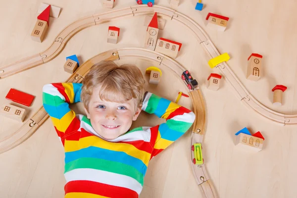 Piccolo bambino biondo che gioca con treni ferroviari in legno al coperto — Foto Stock