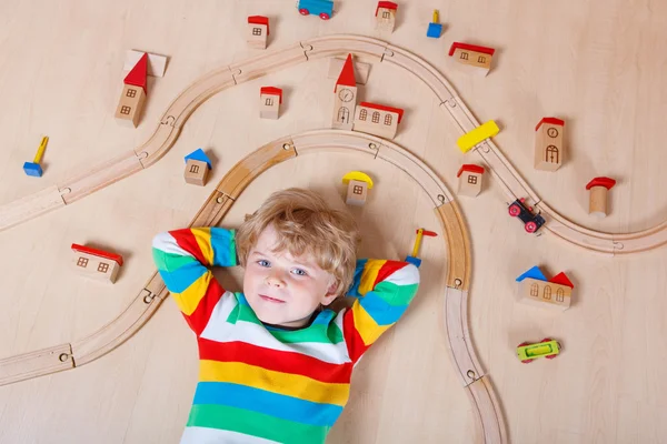 Pequena criança loira brincando com ferrovia de madeira interior — Fotografia de Stock