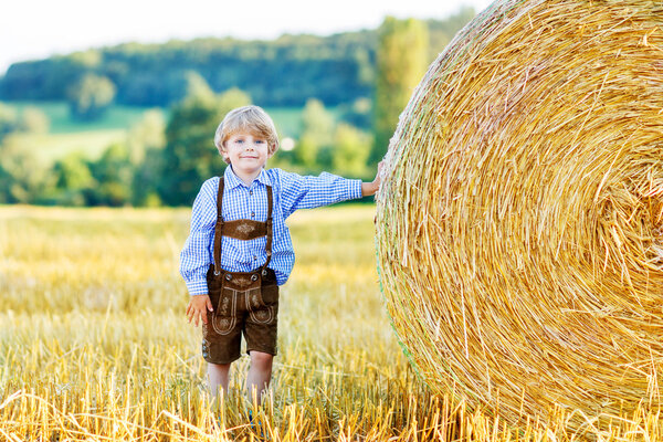 Adorable little kid boy having fun with hay stack on wheat field