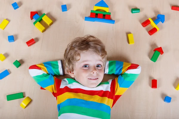 Piccolo bambino biondo che gioca con blocchi di legno colorati al coperto — Foto Stock