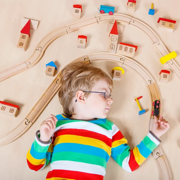 Маленький блондин играет с деревянными поездами в помещении — стоковое фото