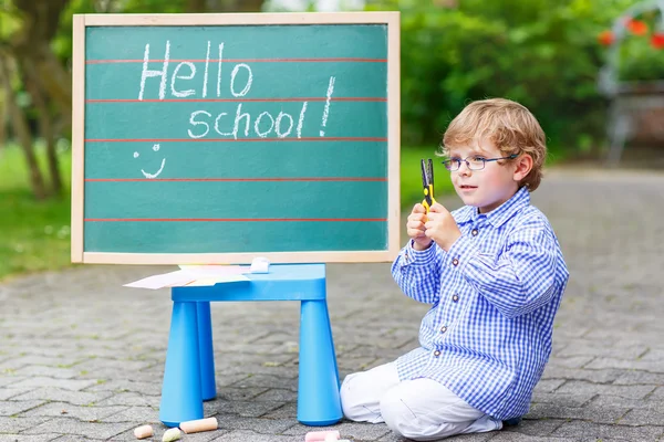 Petit garçon mignon avec des lunettes au tableau noir pratiquant l'écriture — Photo