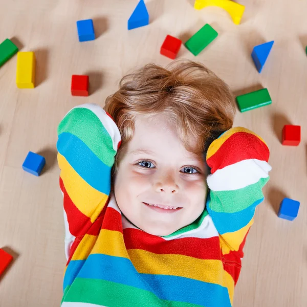 Piccolo bambino biondo che gioca con blocchi di legno colorati al coperto — Foto Stock