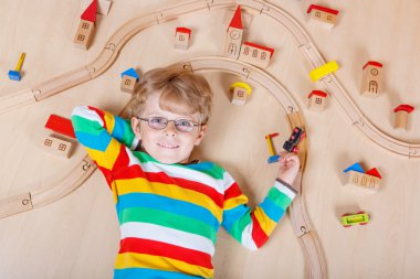 Little blond child playing with wooden railroad trains indoor