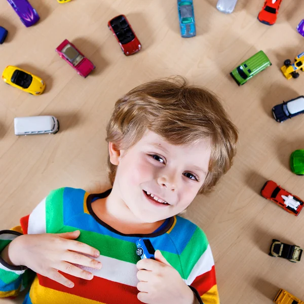Precioso niño rubio jugando con un montón de coches de juguete interior —  Fotos de Stock