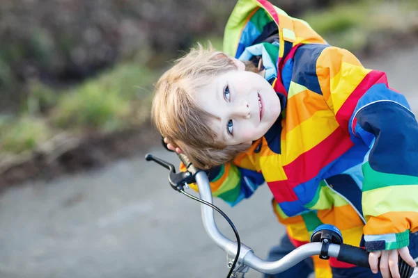 Kid jongen in veiligheidshelm en kleurrijke regenjas rijden fiets, outd — Stockfoto