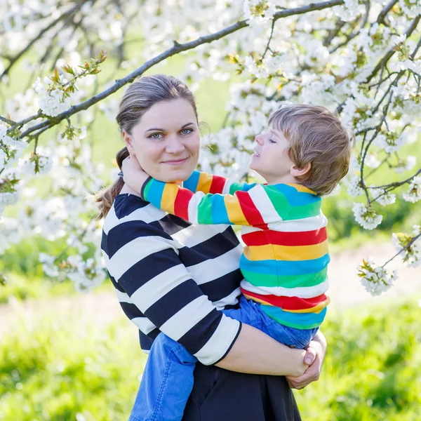 Ung mamma och Lille unge pojken i blommande trädgård — Stockfoto