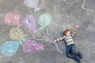 Çocuk renkli balonlarla eğleniyor tebeşirle çiziyor.