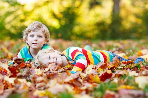 Dos niños pequeños que yacen en hojas de otoño con ropa colorida —  Fotos de Stock