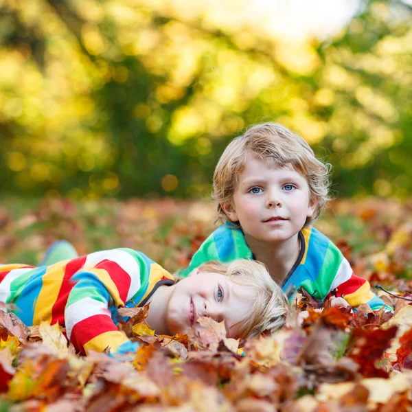 Twee kid weinig jongens leggen in herfst bladeren in kleurrijke kleding — Stockfoto