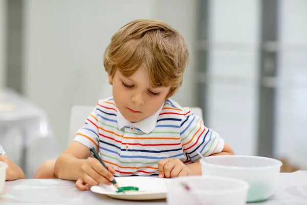 Piccolo ragazzo biondo che mescola diversi colori e pittura — Foto Stock
