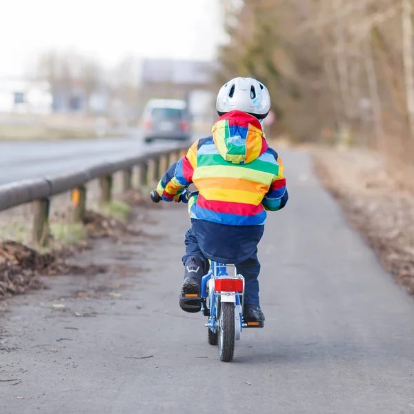 Kid jongen in veiligheidshelm en kleurrijke regenjas rijden fiets, outd — Stockfoto