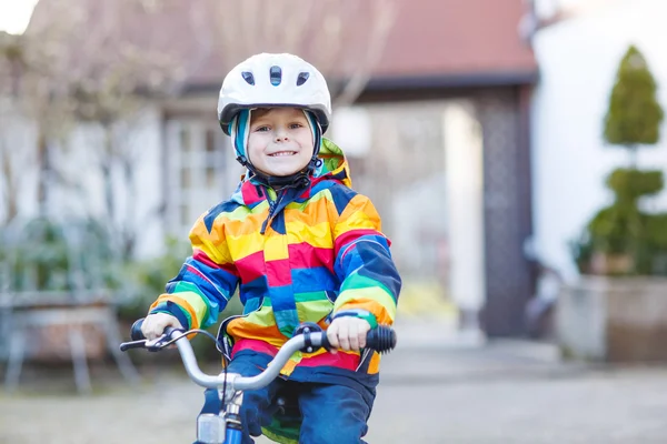 Kid jongen in veiligheidshelm en kleurrijke regenjas rijden fiets, outd — Stockfoto