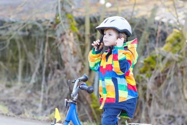 Kid boy in safety helmet and colorful raincoat riding bike, outd — Stock Photo, Image