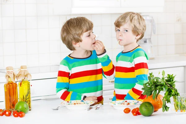 Dvě malé dítě chlapce jíst špagety v domácí kuchyni. — Stock fotografie