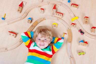 Little blond child playing with wooden railroad trains indoor