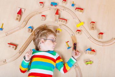 Little blond child playing with wooden railroad trains indoor