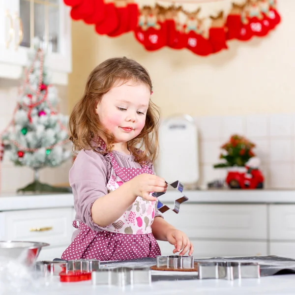 Маленькая девочка печет пряничное печенье на домашней кухне — стоковое фото