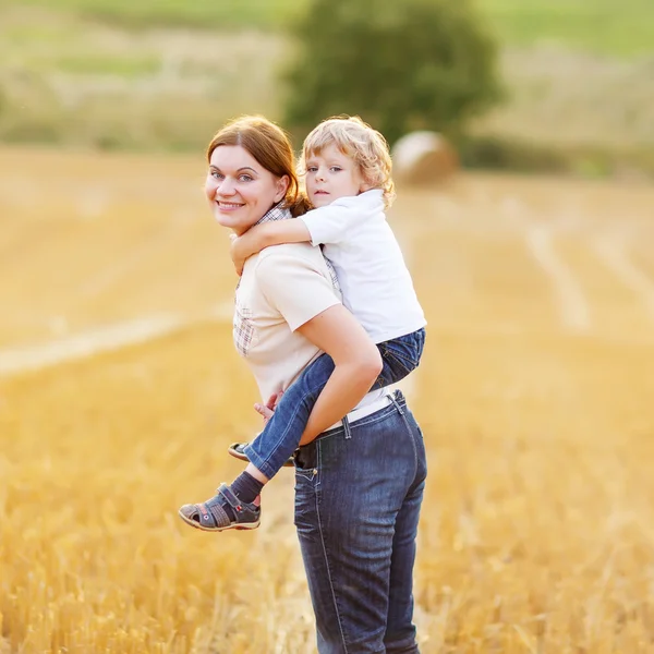 Young mother and her little son having fun on yellow hay field — Stock Photo, Image