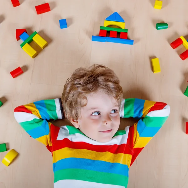 Petit enfant blond jouant avec des blocs de bois colorés à l'intérieur — Photo