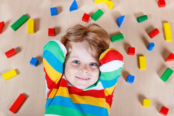 Piccolo bambino biondo che gioca con blocchi di legno colorati al coperto — Foto Stock