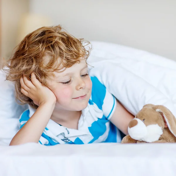 Entzückendes Kind Junge nach dem Schlafen in seinem weißen Bett mit Spielzeug — Stockfoto