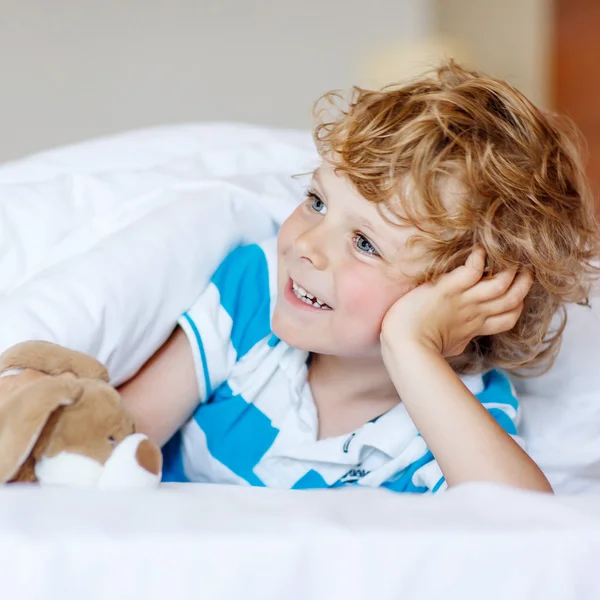 Entzückendes Kind Junge nach dem Schlafen in seinem weißen Bett mit Spielzeug — Stockfoto