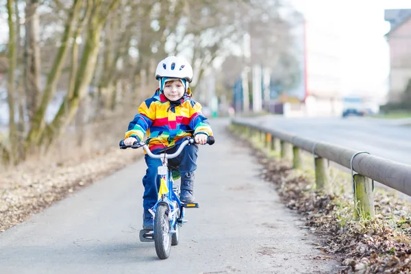 Kid jongen in veiligheidshelm en kleurrijke regenjas rijden fiets, outd — Stockfoto